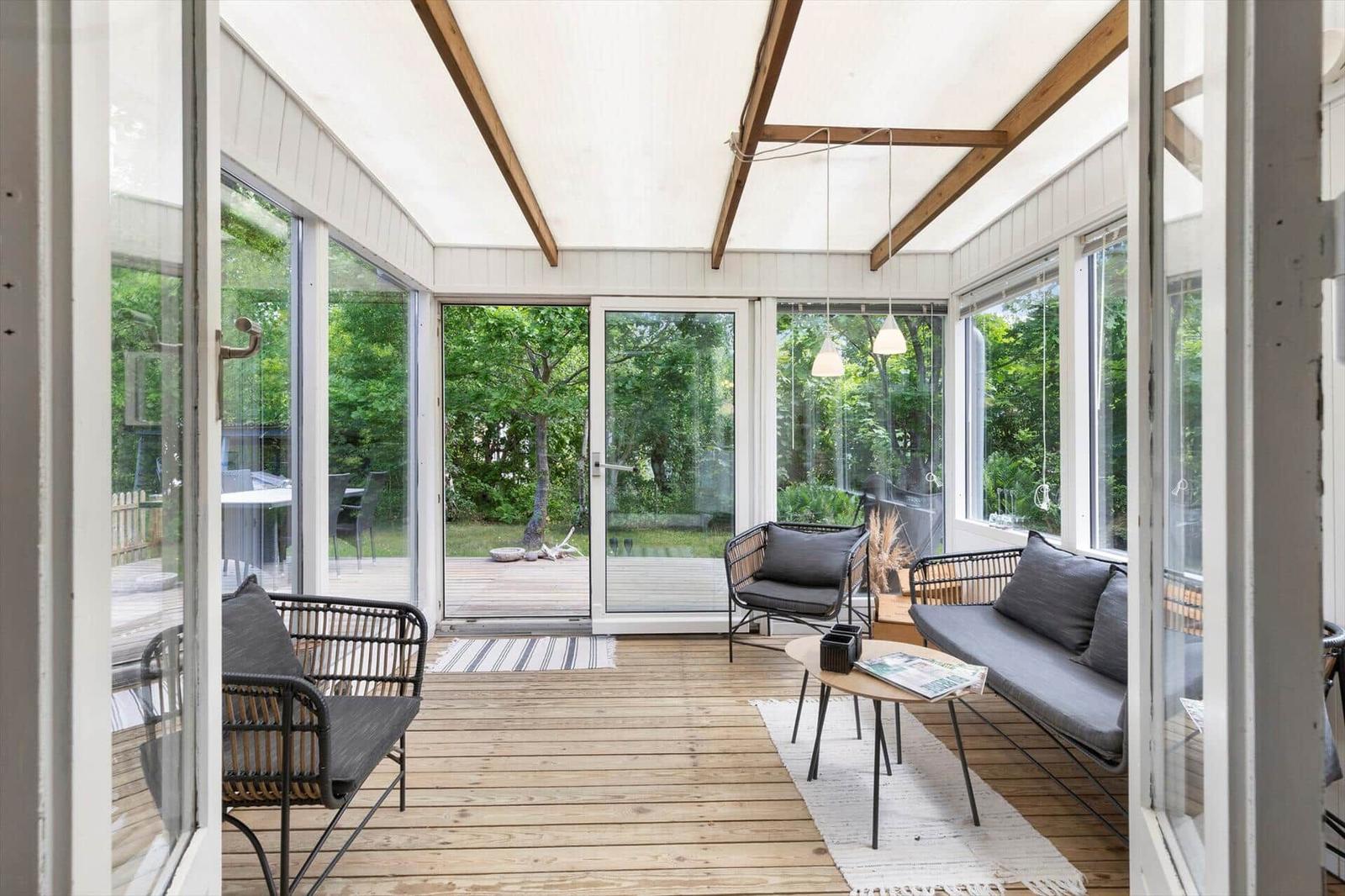 Interior with glass walls, wooden floor, and seating. View of green garden.