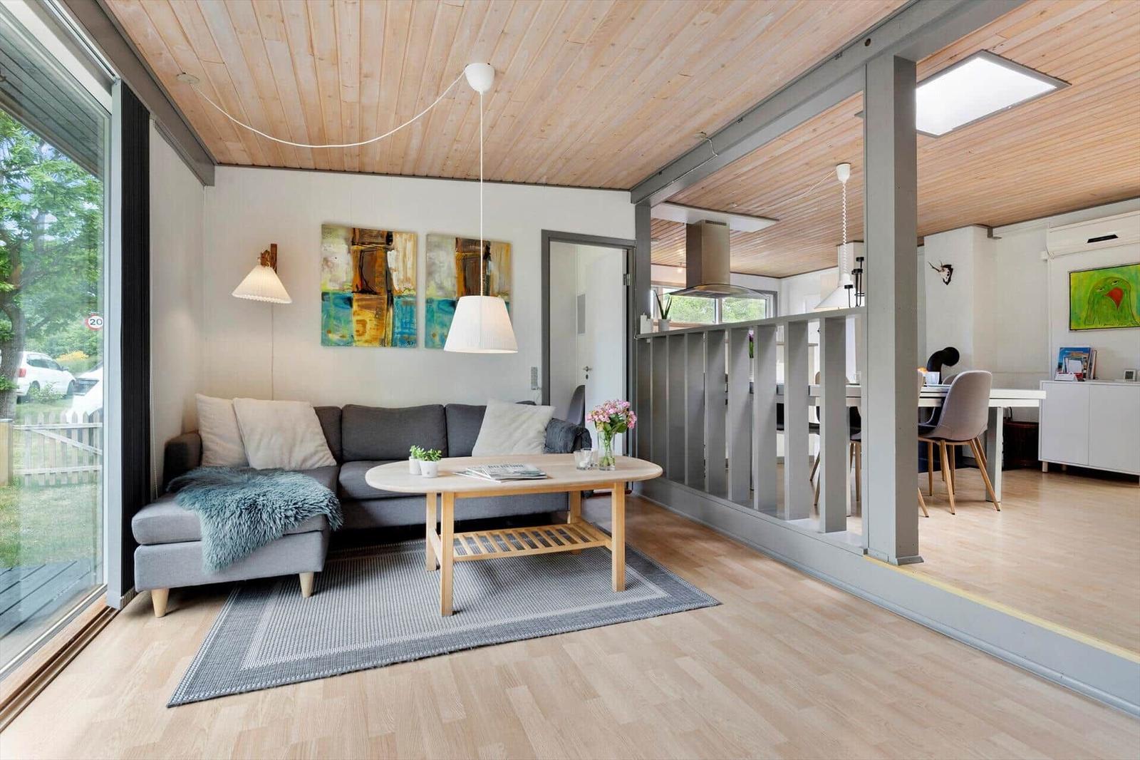 Living room with sofa, table, and balcony view. Kitchen in background.