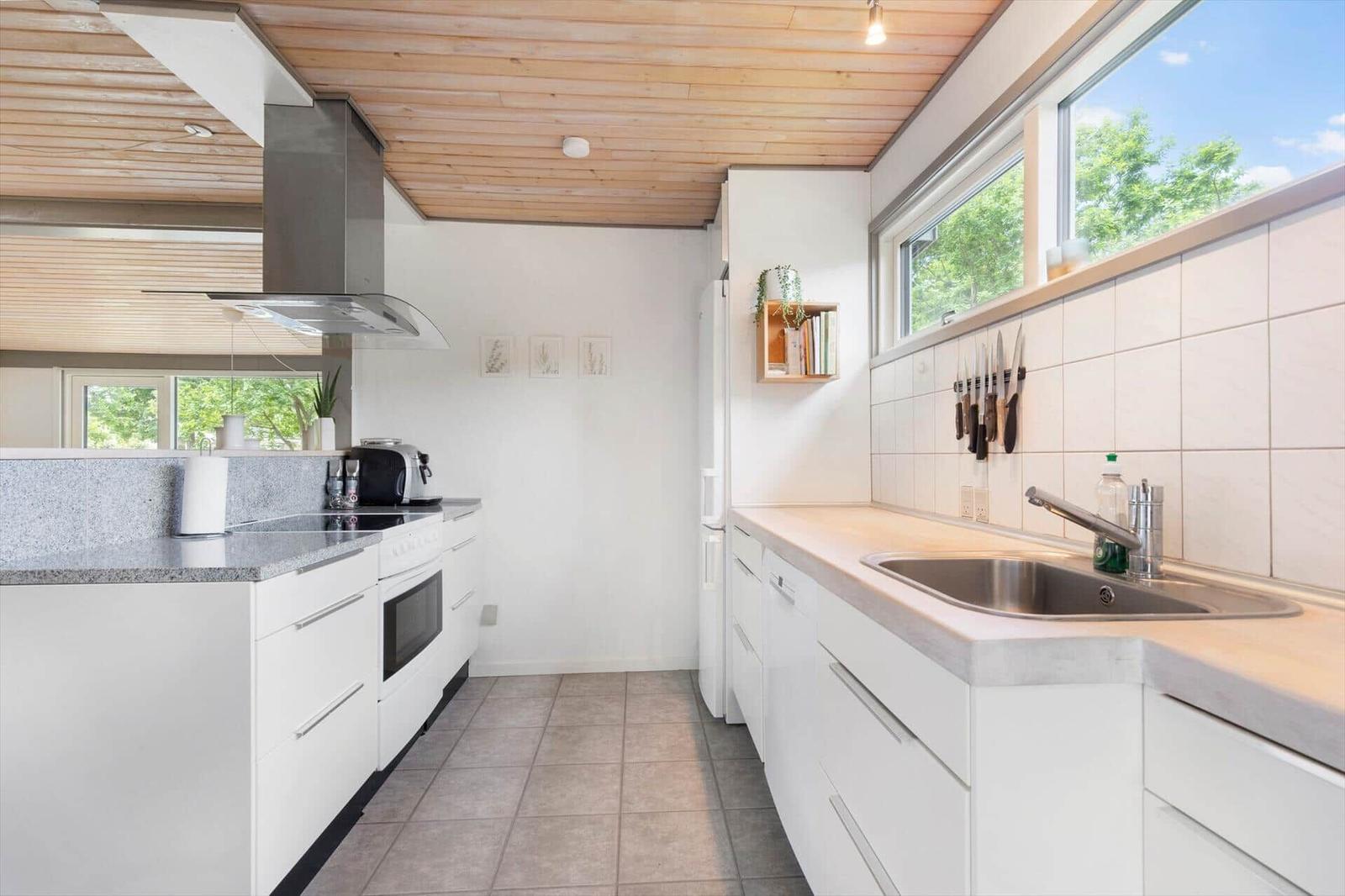 Modern kitchen with white cabinets, stainless steel sink, and wooden ceiling.