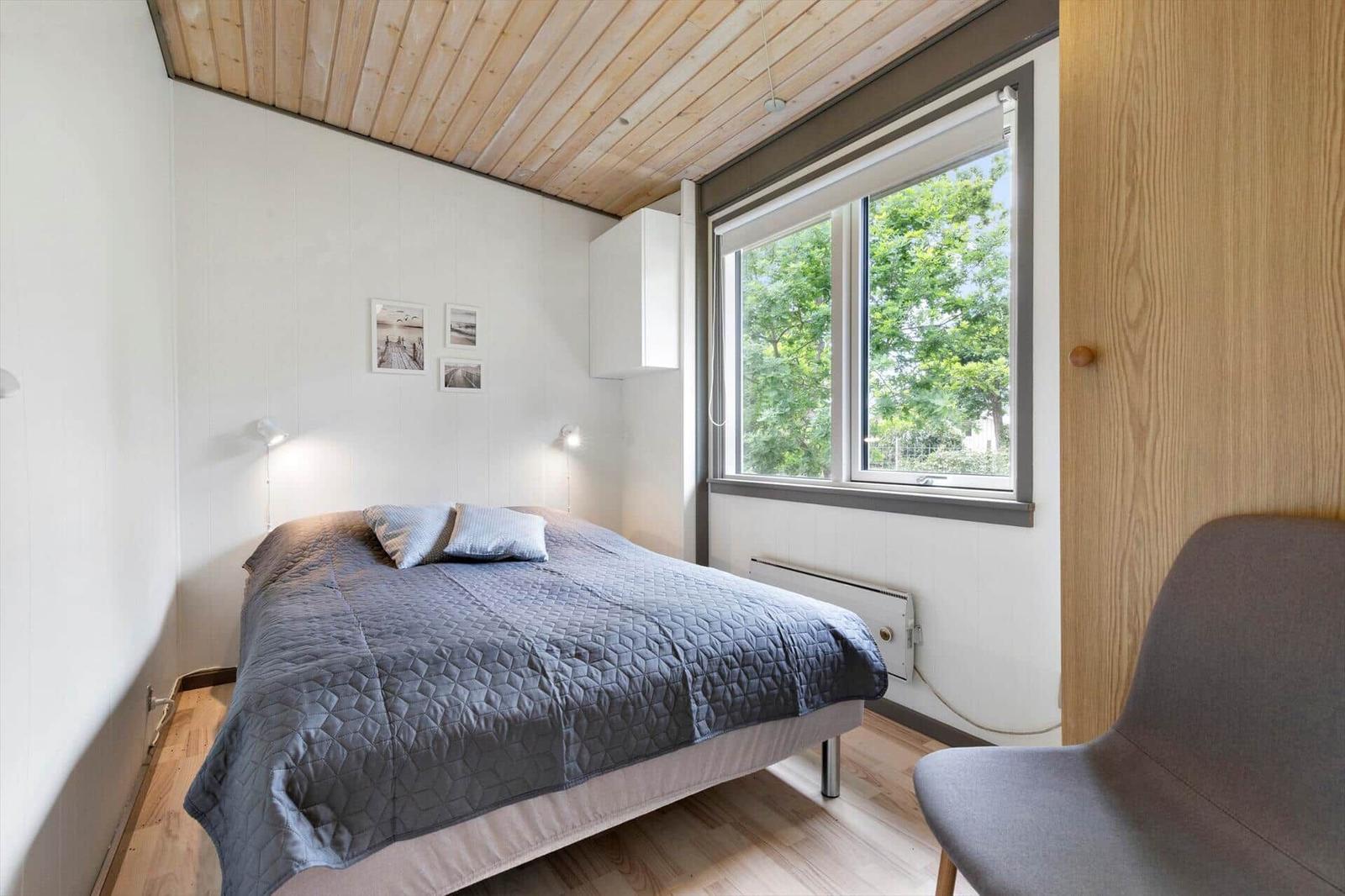 Bedroom with bed, window, and chair. Wooden ceiling and white walls.