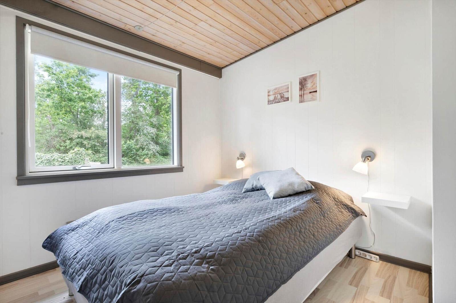 Bedroom with bed, window, and wall lamps.