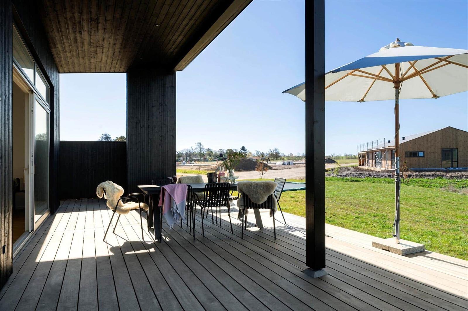 Terrasse mit Tisch, Stühlen und Sonnenschirm. Blick auf grünen Garten und Ferienhaus.
