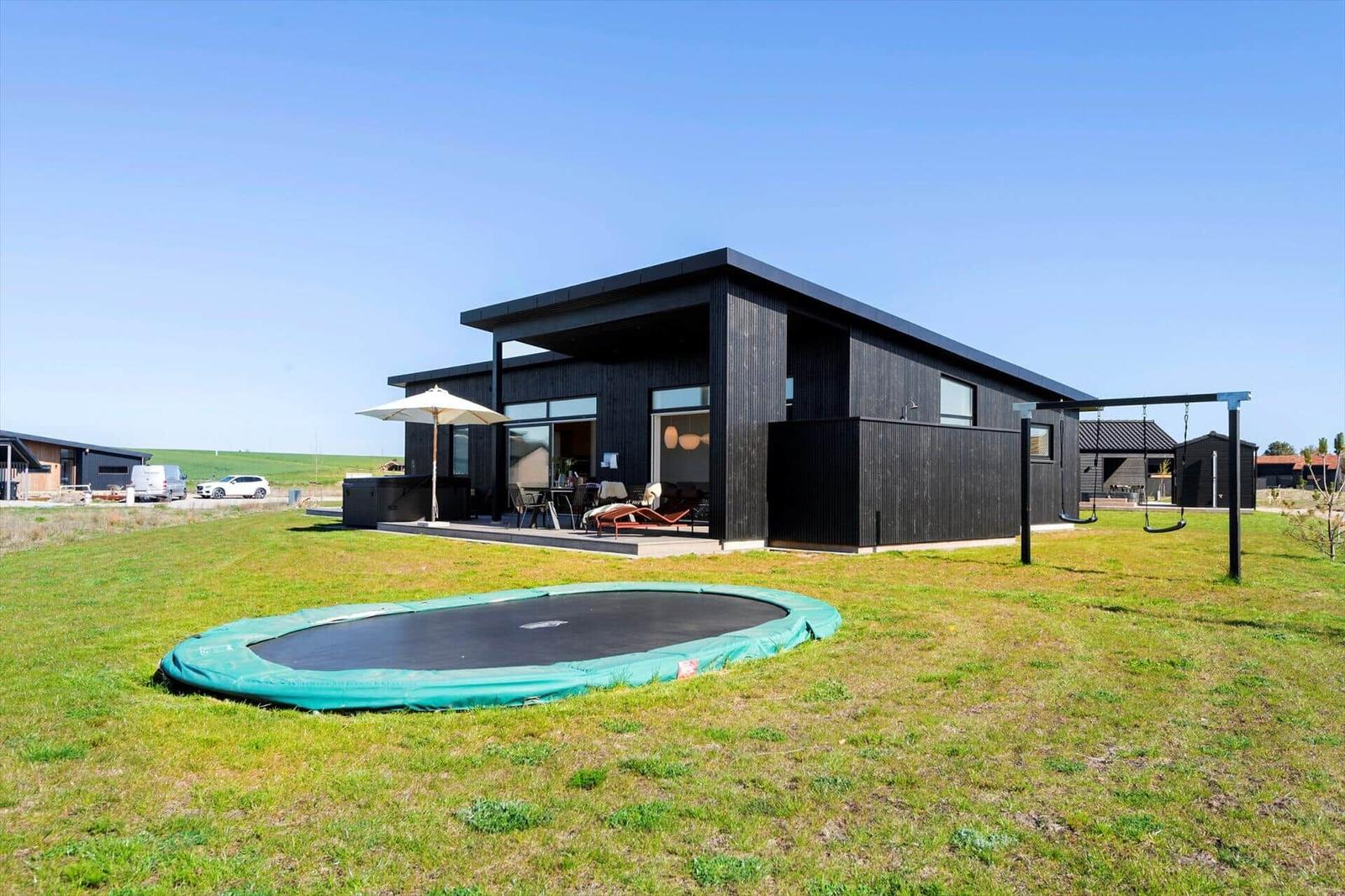 Moderne Villa mit Terrasse, Trampolin und Spielplatz auf grünem Grundstück.
