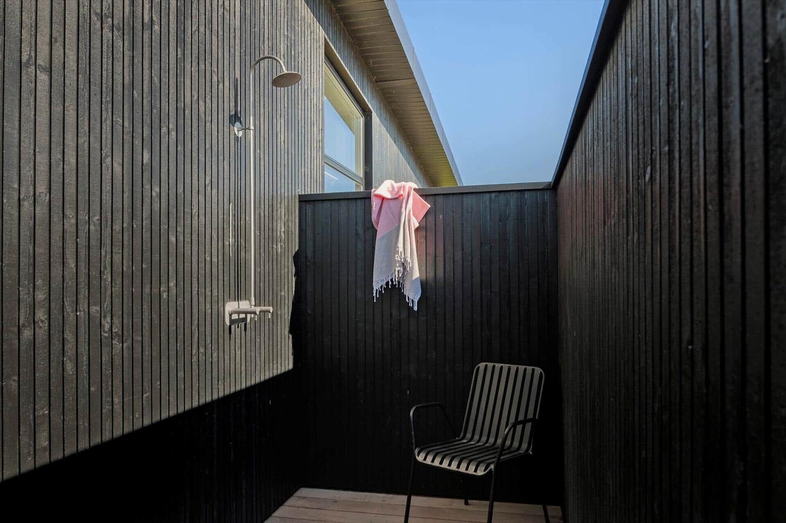 Außendusche mit Stuhl und Handtuch an schwarzer Holzwand.