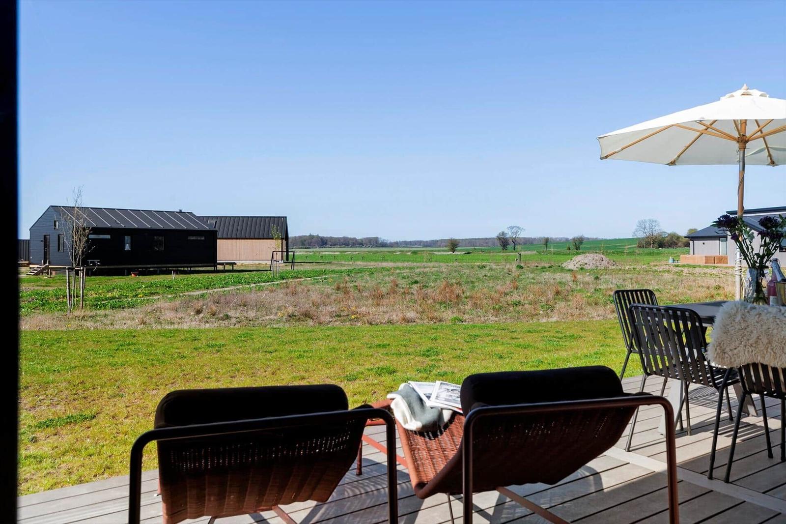 Terrasse mit Sitzgelegenheiten und Blick auf Felder und Gebäude.