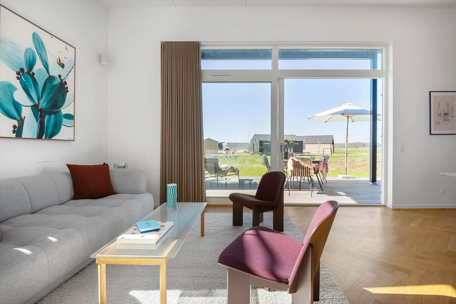 Wohnzimmer mit Sofa, Tisch und Stühlen. Durchgang zur Terrasse mit Sonnenschirm.