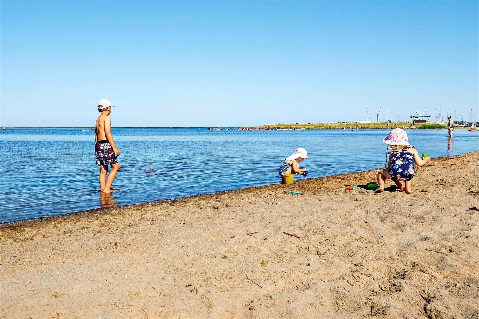 Two people wade in shallow water, a boat sails through a canal.