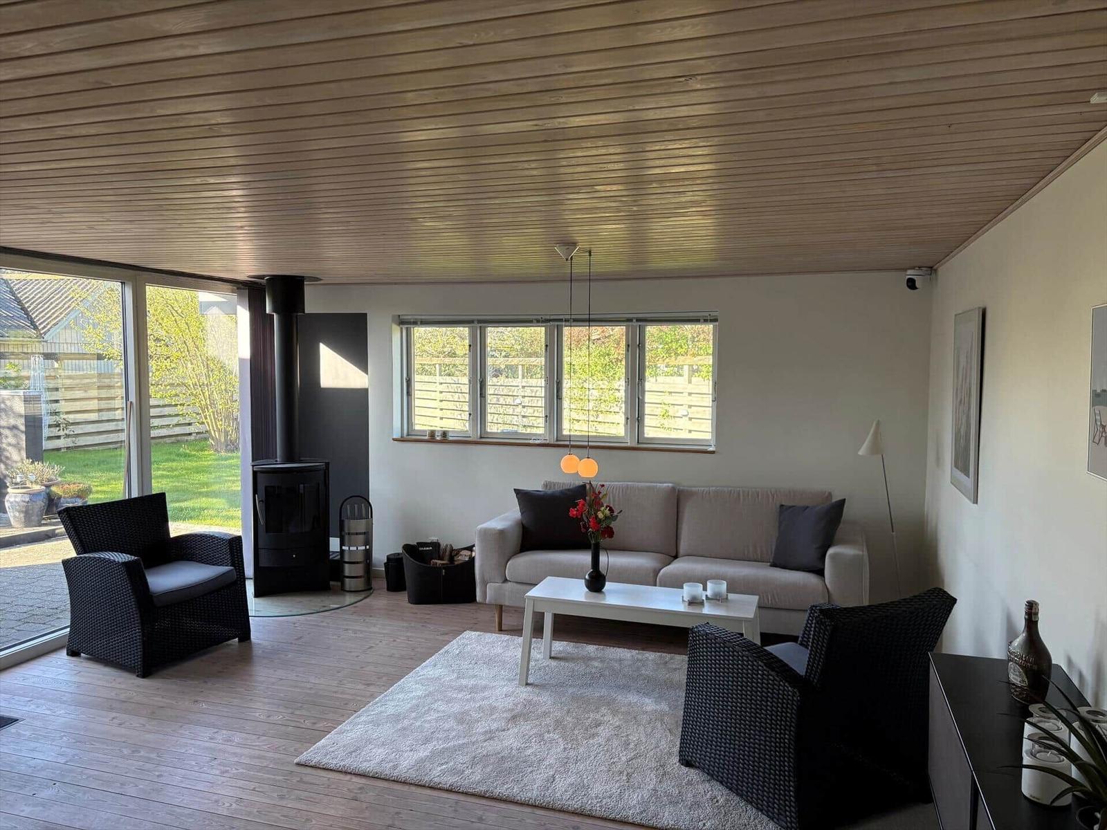 Wohnzimmer mit Sofa, zwei Sesseln, Kamin und Blick auf Garten.