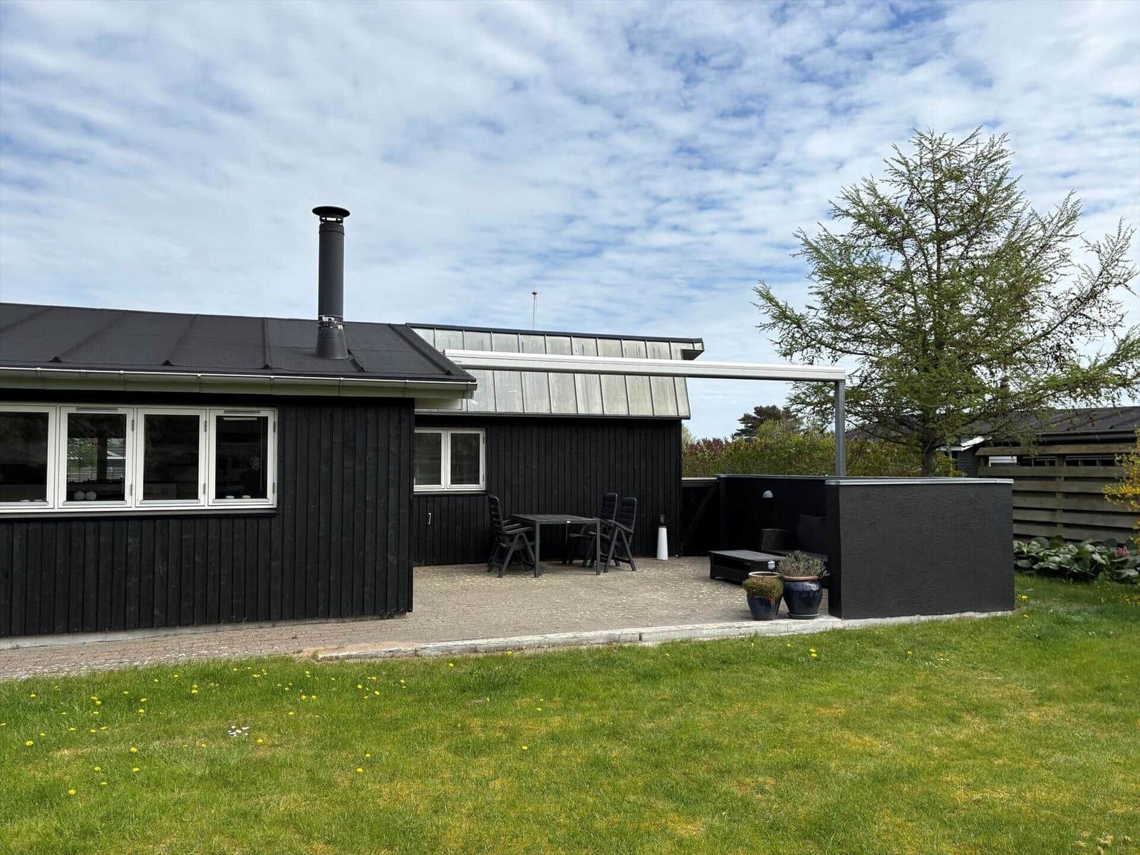 Schwarzes Haus mit Terrasse, Garten und Grillbereich unter freiem Himmel.