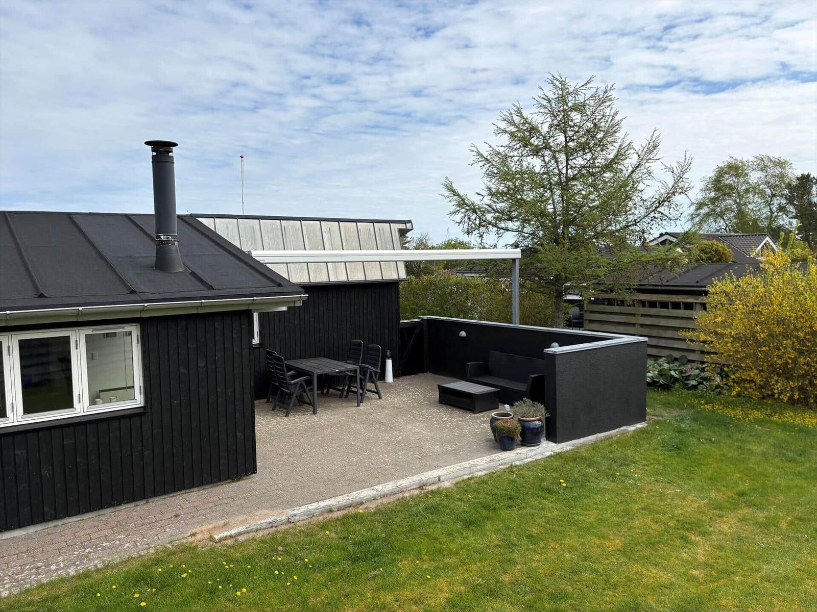Hinterhof mit Terrasse, Tisch, Stühlen und Sitzbank. Schwarze Holzfassade und grüner Rasen.