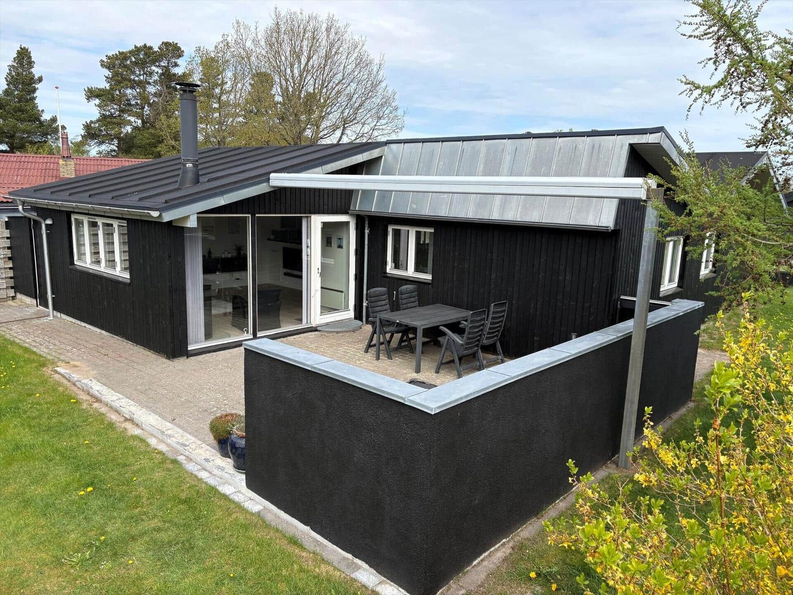 Schwarzes Haus mit Terrasse und Garten. Glastüren führen ins Innere.