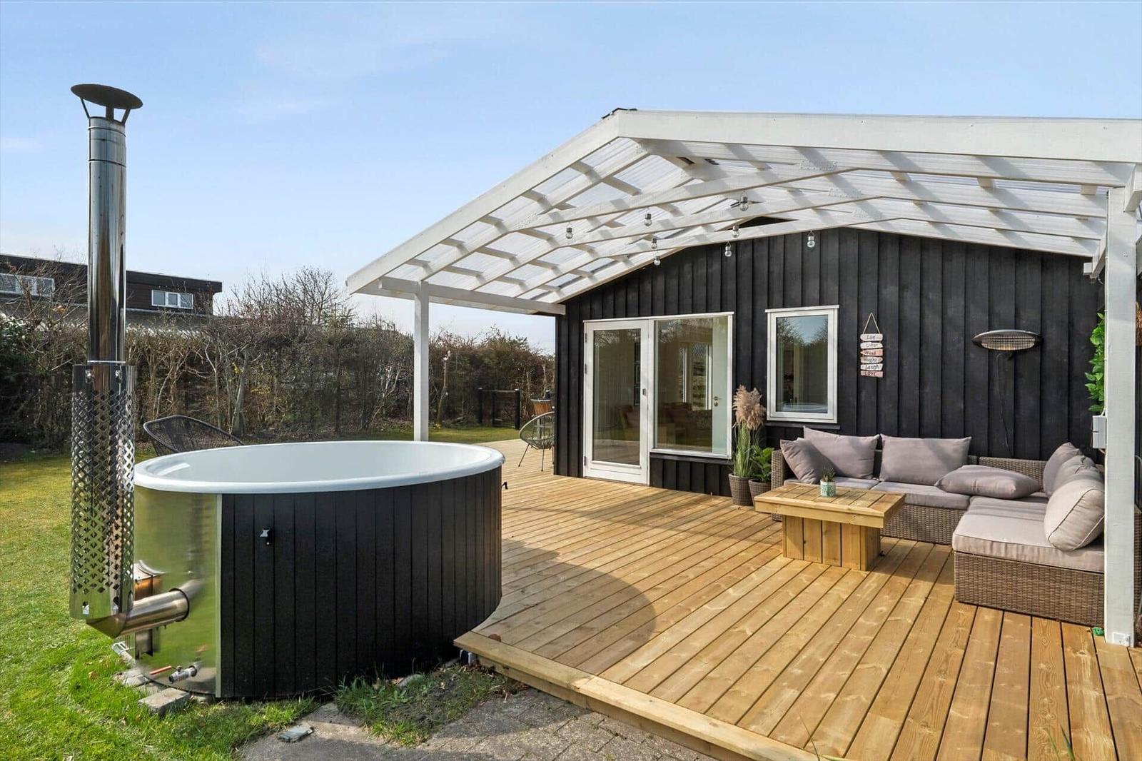 Outdoor area with hot tub, seating group, and wooden deck under a white pergola.