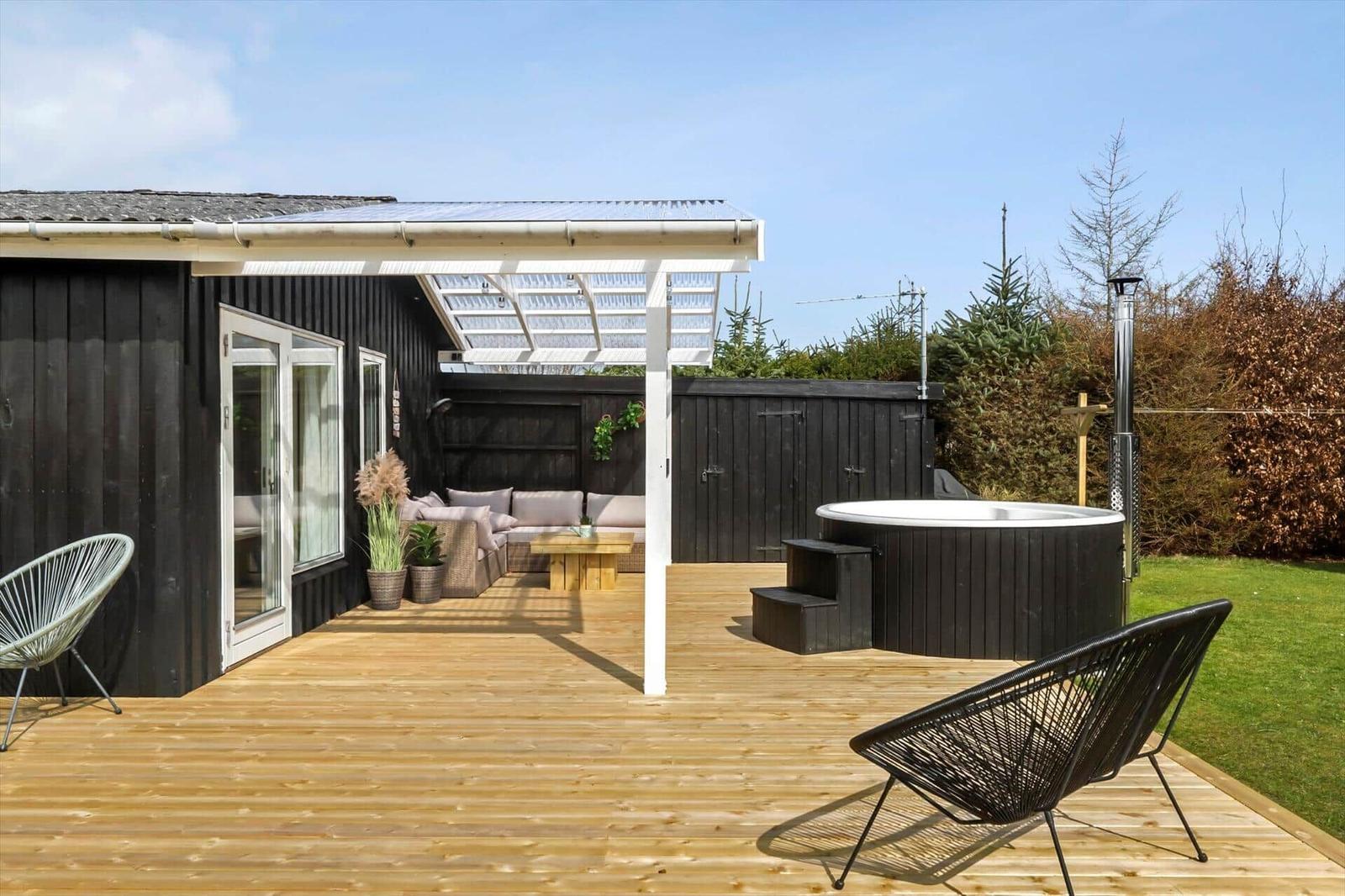 Deck with hot tub, seating area, and lawn. Black wood walls and wooden planks.