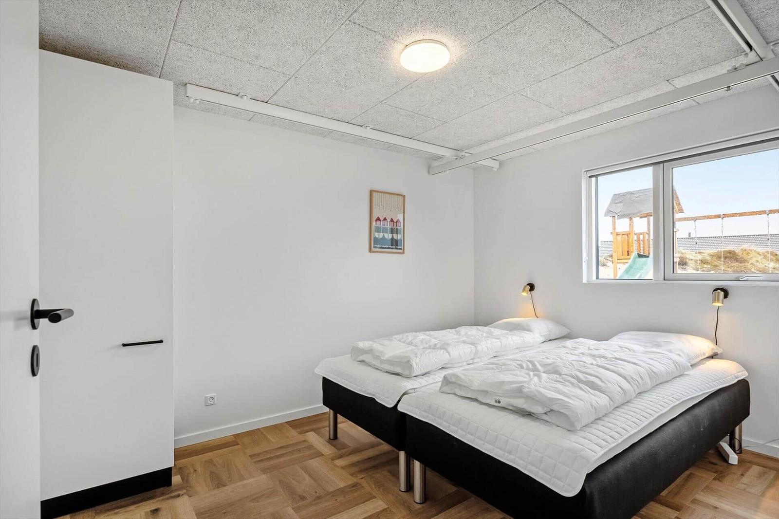 Schlafzimmer mit Doppelbett, Holzboden und Fenster zum Außenbereich.