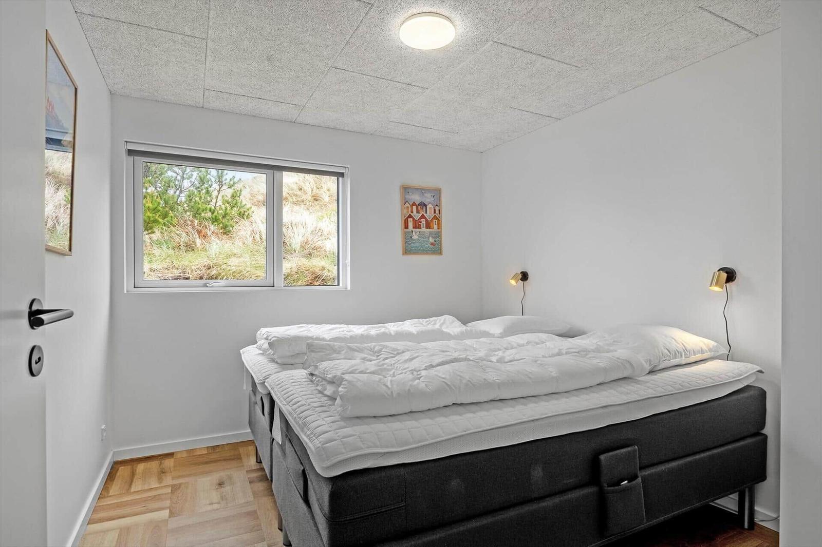 Schlafzimmer mit Bett, Fenster und Wandlampen. Holzfußboden und weiße Wände.
