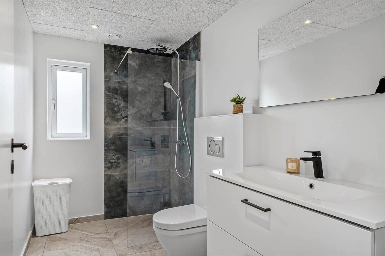 Badezimmer mit Dusche, Waschbecken und Toilette. Weiße Fliesen und moderne Einrichtung.