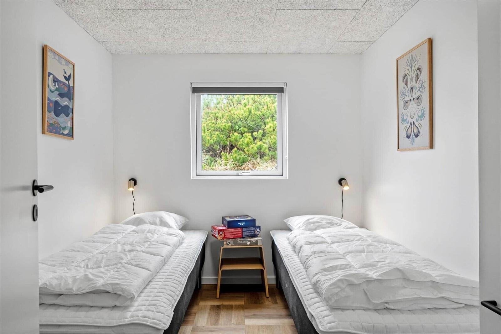 Zwei Einzelbetten mit weißen Bettwäschen, kleiner Holztisch und Fenster mit Blick auf Grün.