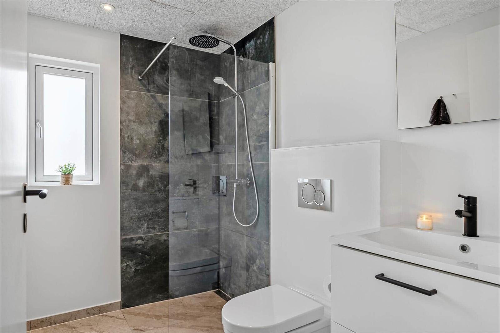 Moderne Badezimmer mit Dusche, Waschbecken und Toilette. Dunkle Fliesen und weißes Design.