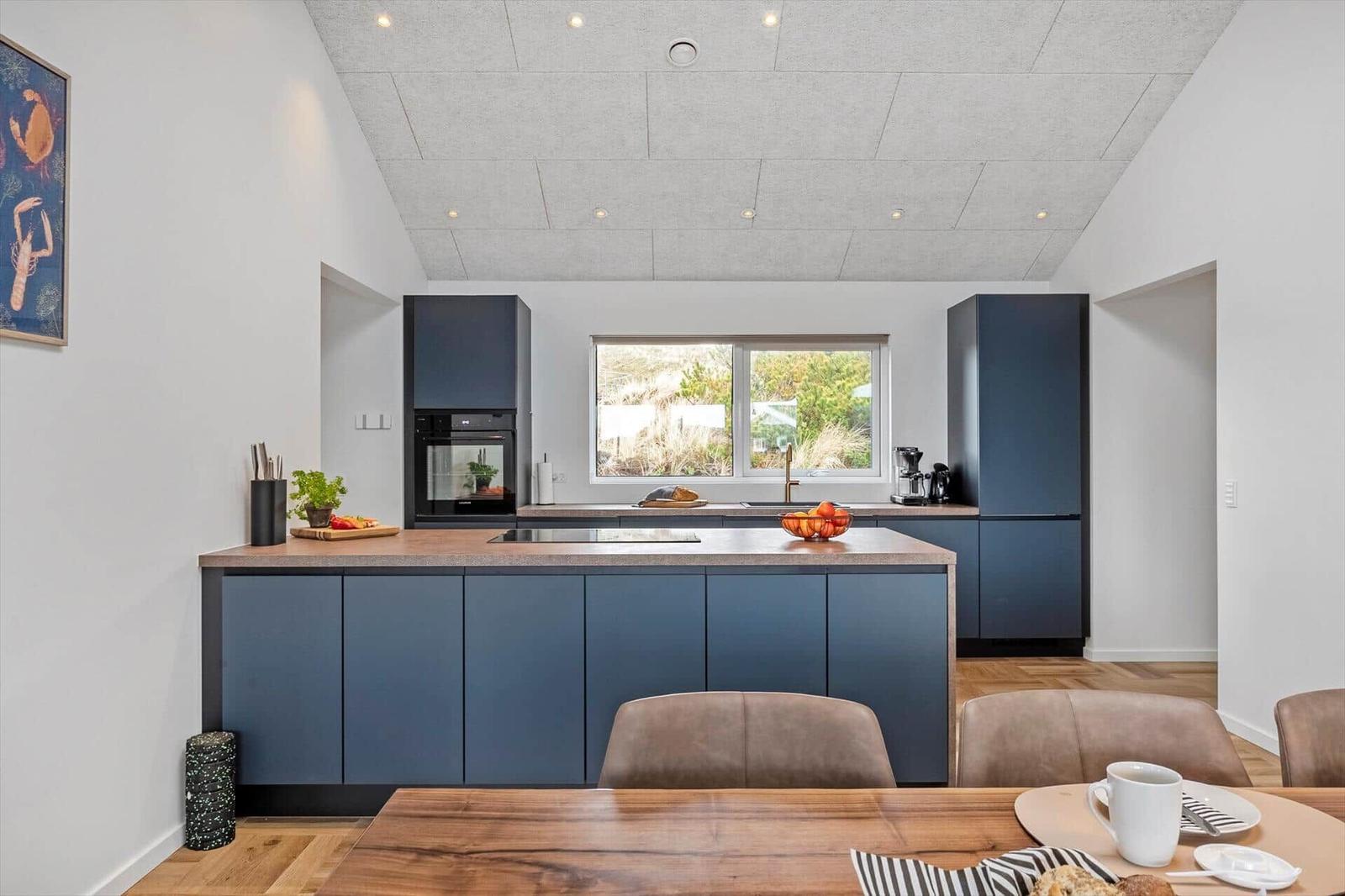 Moderne Küche mit blauen Schränken, Kücheninsel und Fensterblick auf Grünflächen.