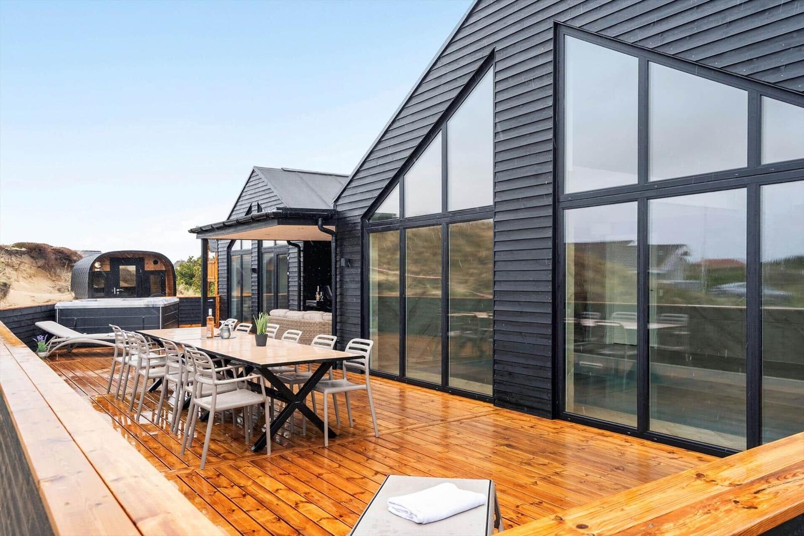 Terrasse mit Tisch, Stühlen und Liege. Hintergrund: modernes Haus mit Glasfassade und Dach.