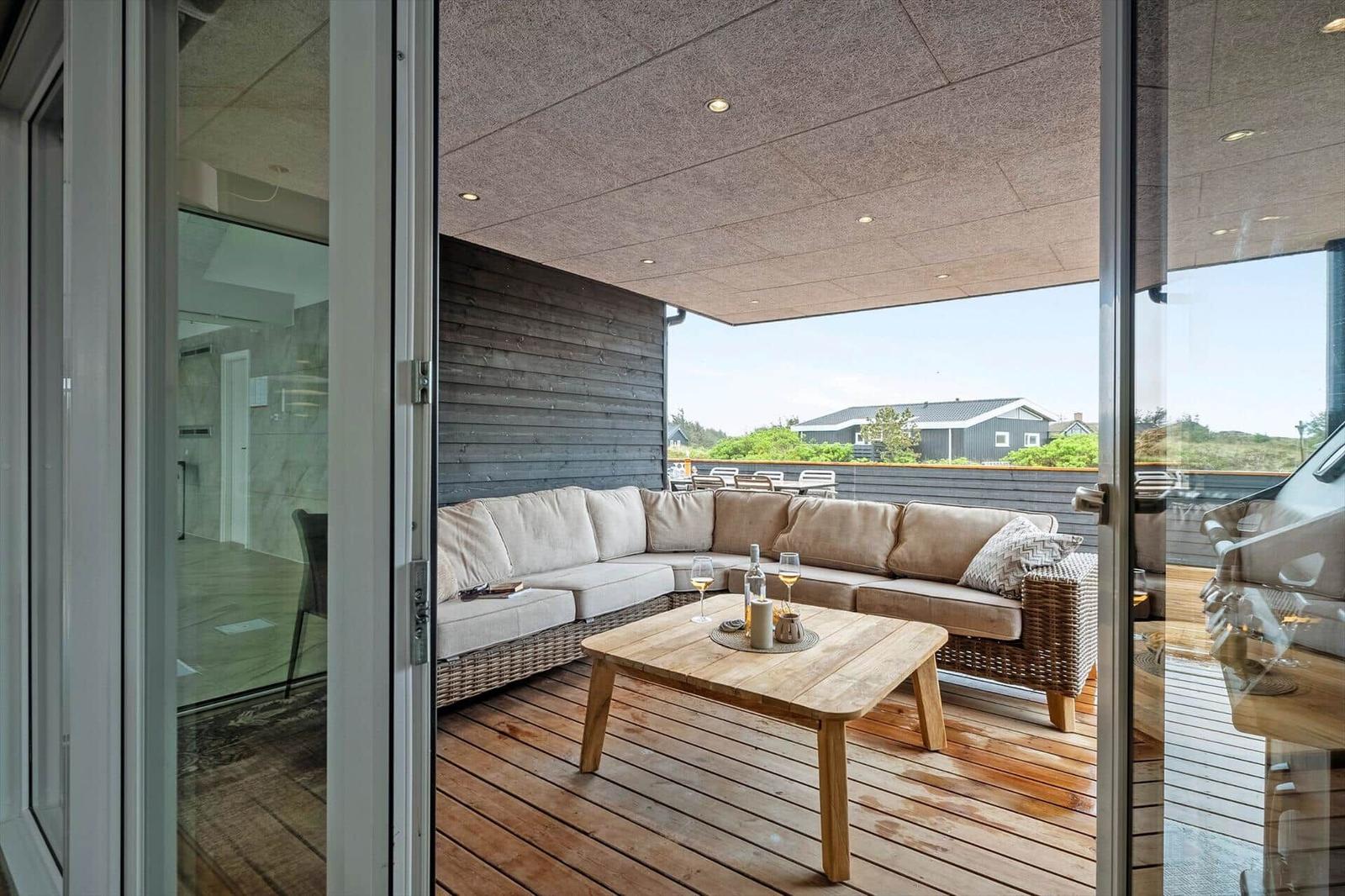 Terrasse mit Sitzgruppe und Holztisch. Blick auf grüne Landschaft und Häuser.