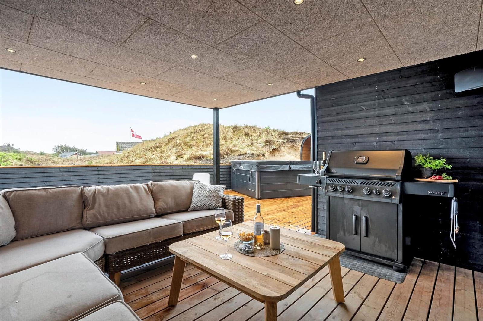 Terrasse mit Sofa, Grill und Whirlpool. Blick auf Dünen und Flagge.
