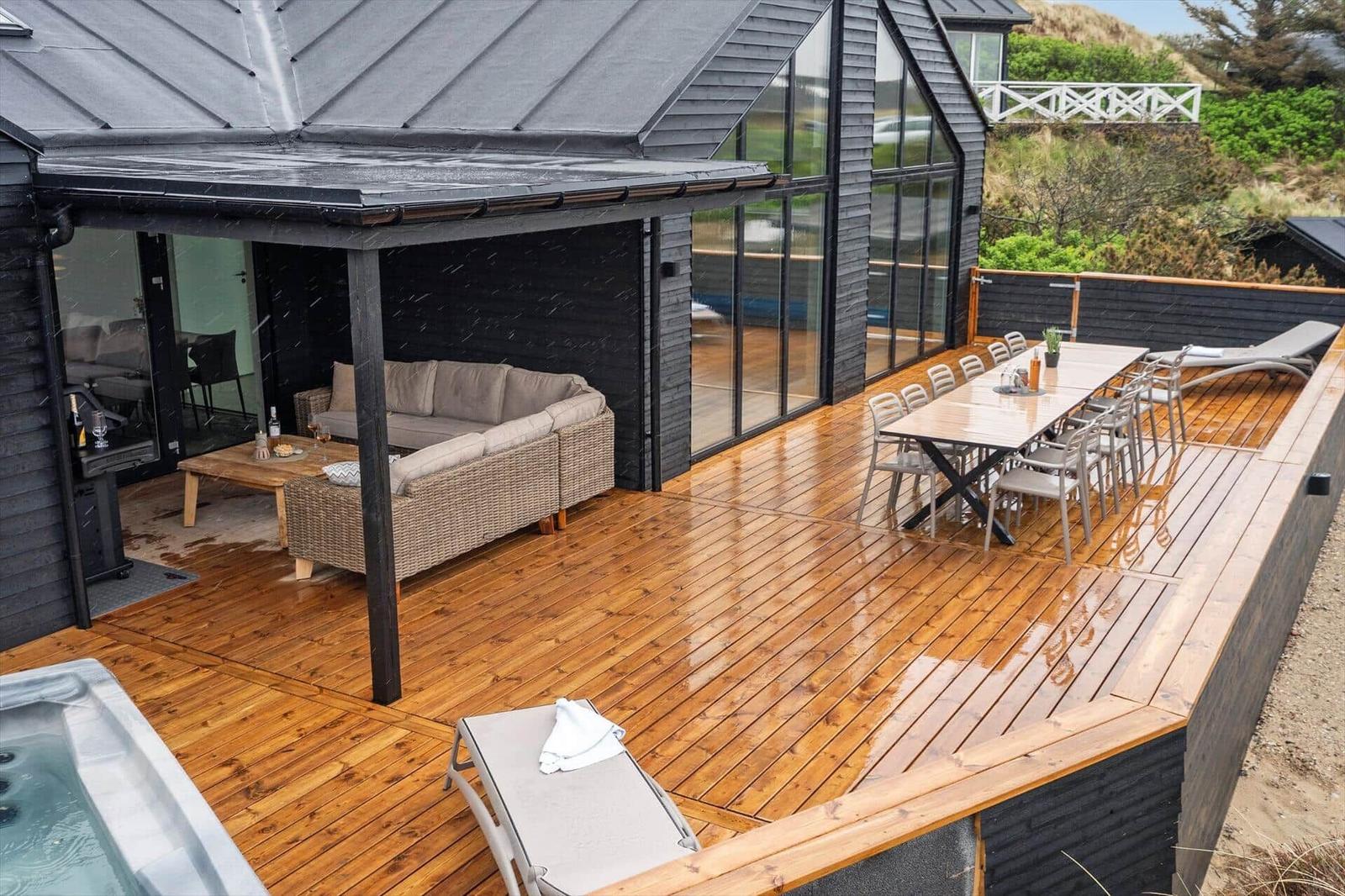 Terrasse mit Holzdecke, Sitzgruppe, Esstisch und Whirlpool. Modernes Haus mit Glasfassade.