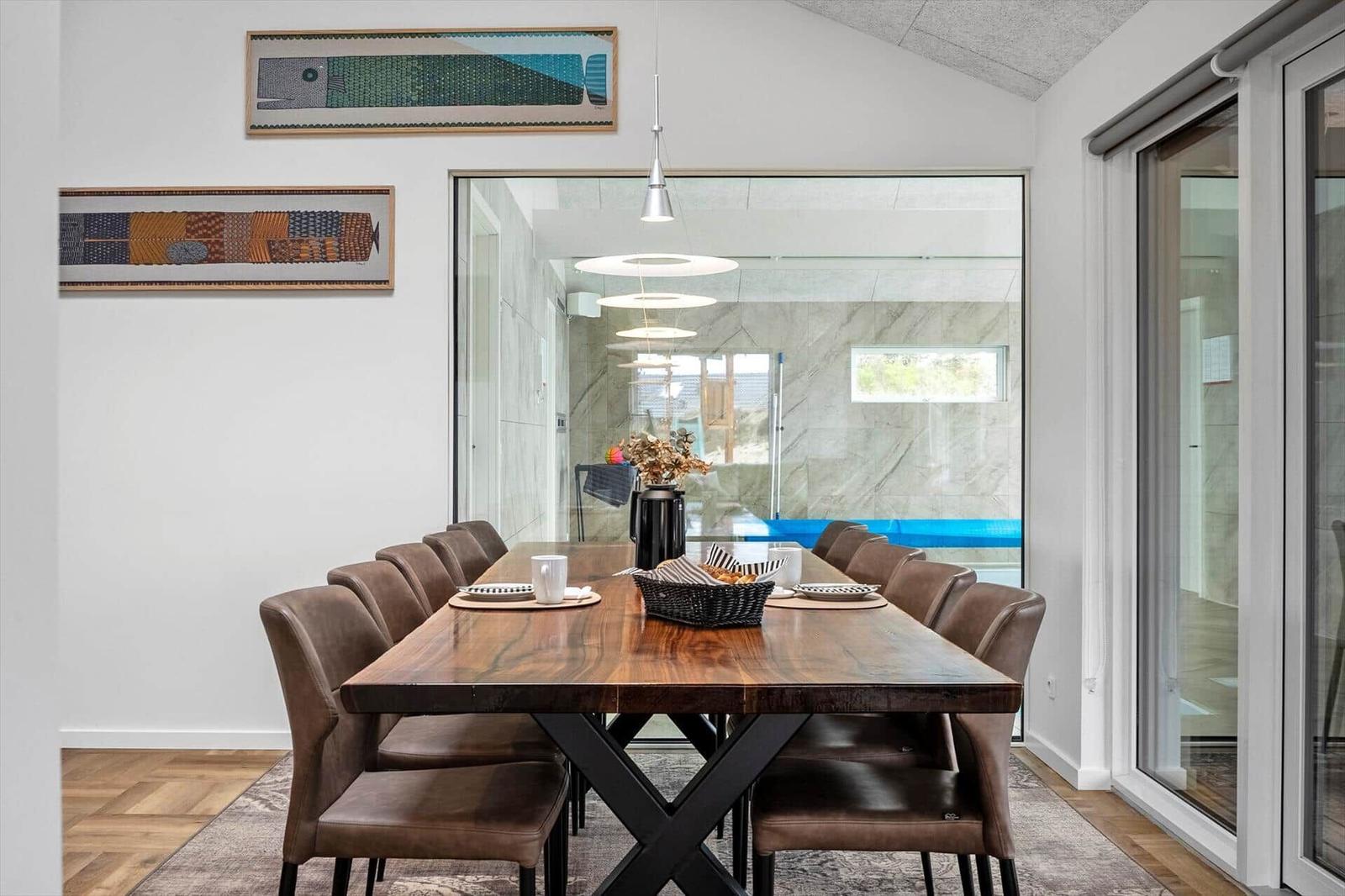 Esszimmer mit langem Holztisch und braunen Stühlen. Glaswand zeigt Poolbereich.