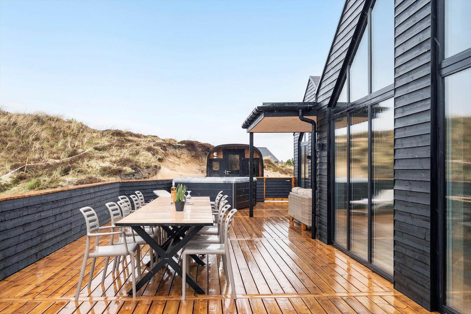 Terrasse mit Tisch und Stühlen, Whirlpool und Blick auf Dünen.