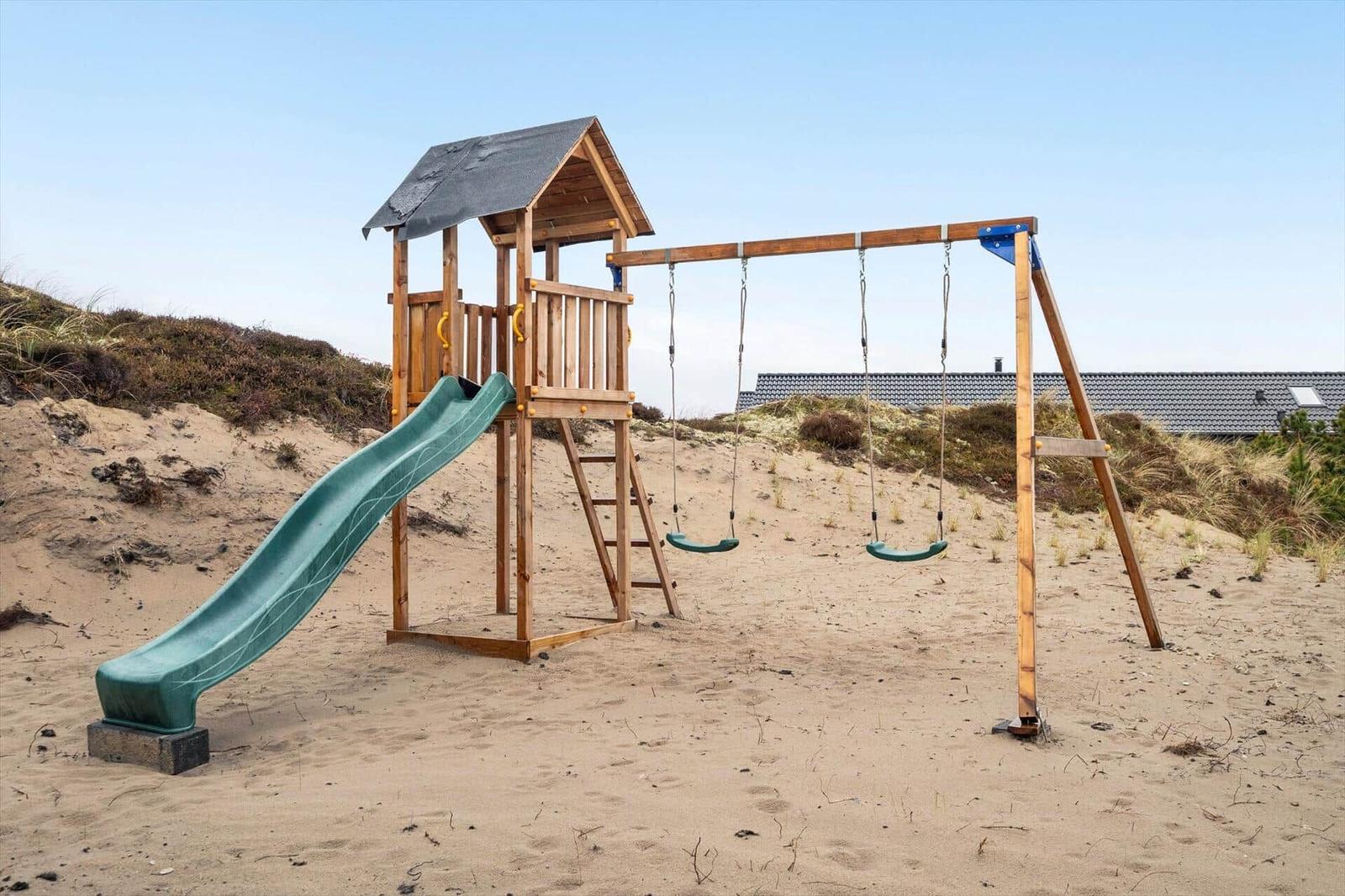 Holzspielplatz mit Rutsche und Schaukel auf sandigem Grund.