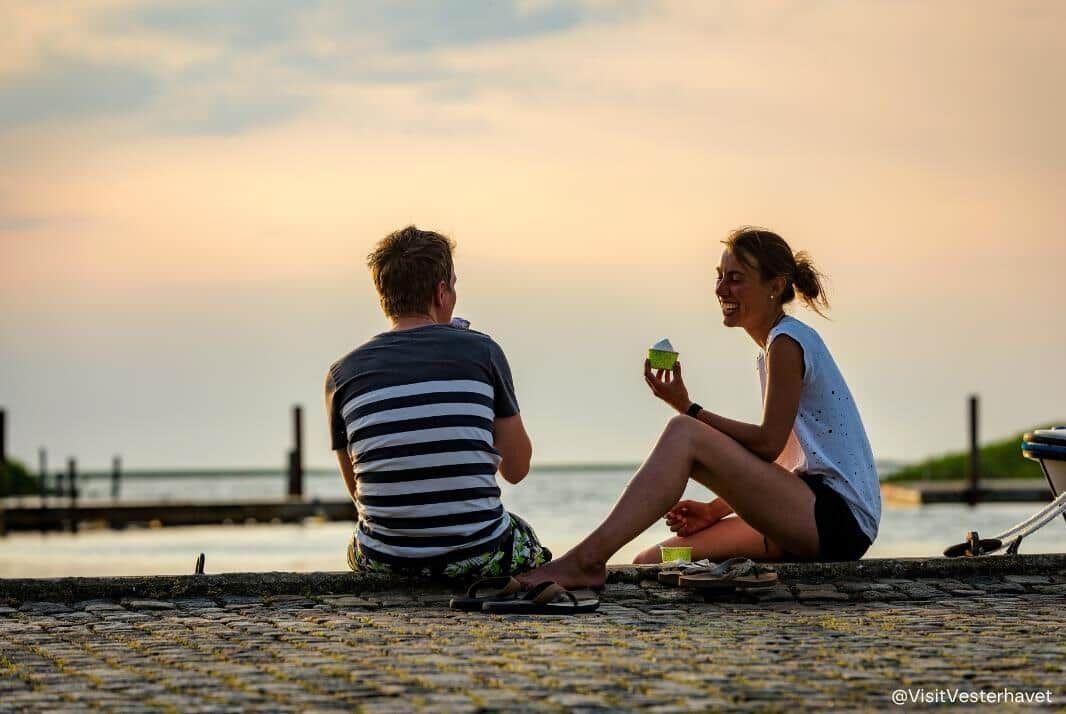 A couple sits by the waters edge enjoying ice cream in the evening.