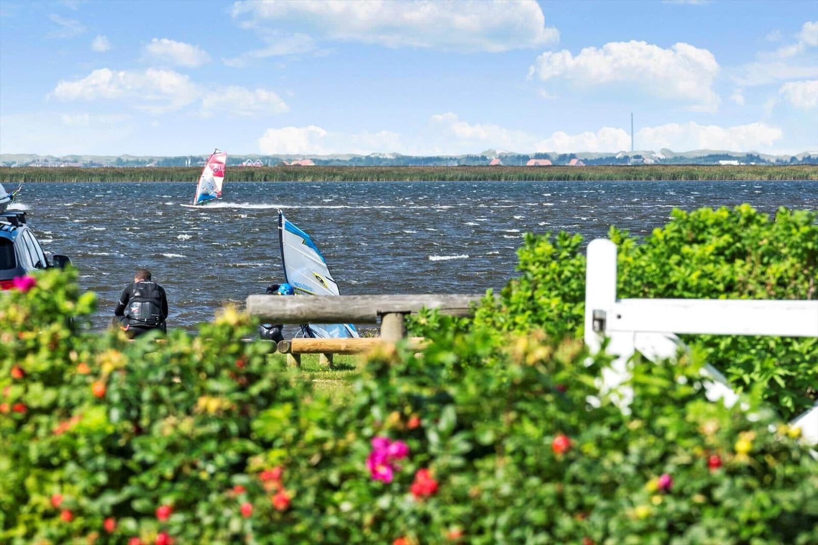 Beach with wooden tables and chairs, grassy area and water under blue sky with white clouds.