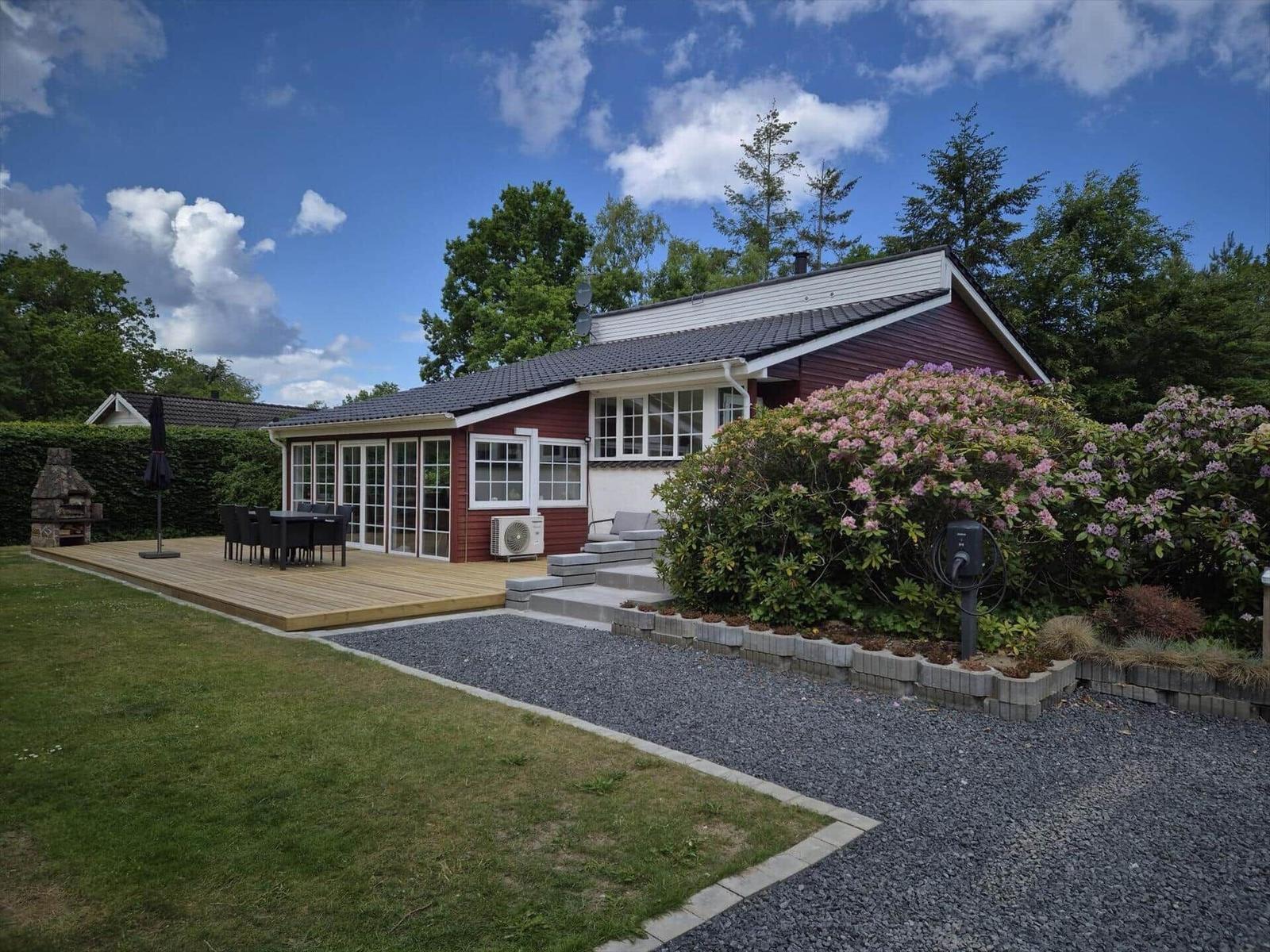 A house with terrace, grill and flower hedges under blue sky.