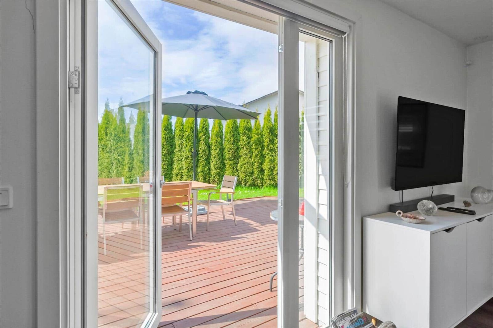 Durch Glastüren ist eine Terrasse mit Tisch, Stühlen und Sonnenschirm zu sehen.