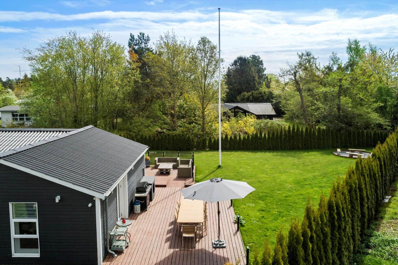 Haus mit Terrasse, Garten und Grillplatz. Umgeben von Bäumen und Hecken.