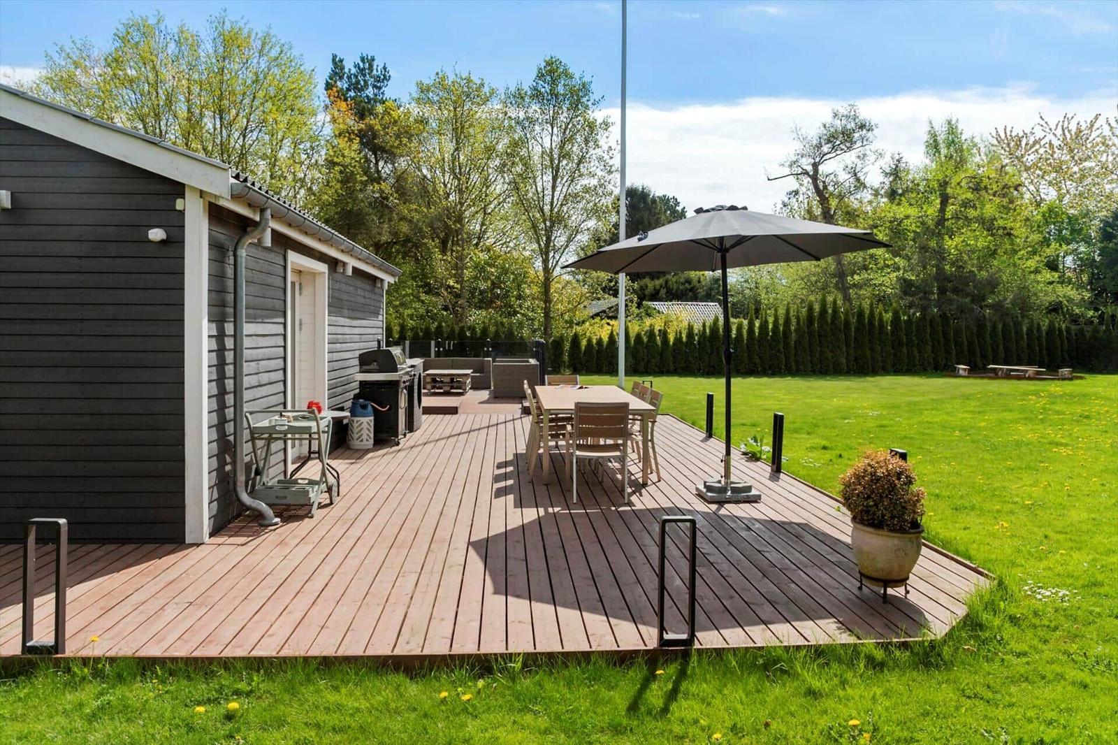 Terrasse mit Tisch, Stühlen und Sonnenschirm neben einem Haus mit Garten.