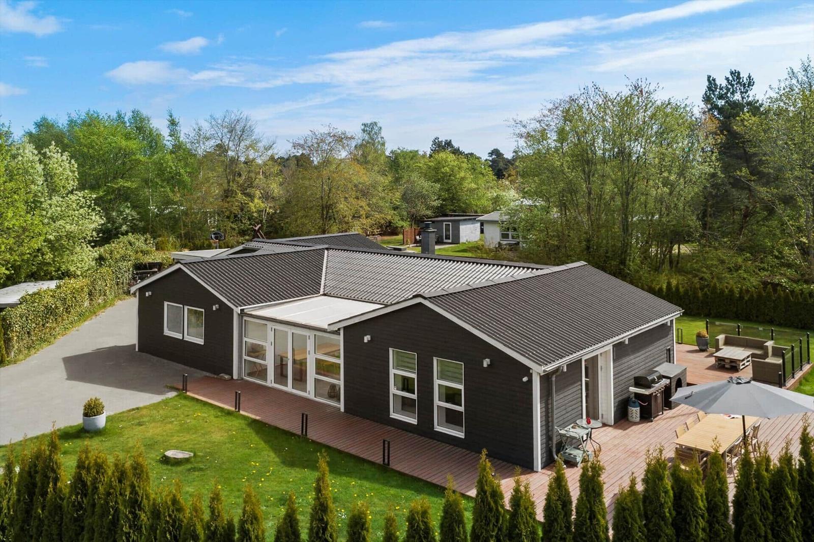 Moderne Villa mit Terrasse, Grill und Garten. Umgeben von Bäumen und Grünflächen.