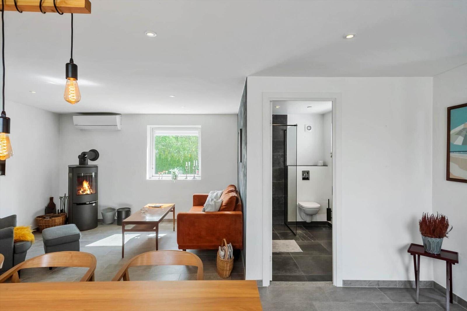 Wohnraum mit Kamin, Sofa und Blick auf Garten. Nebenraum mit Dusche und Toilette.