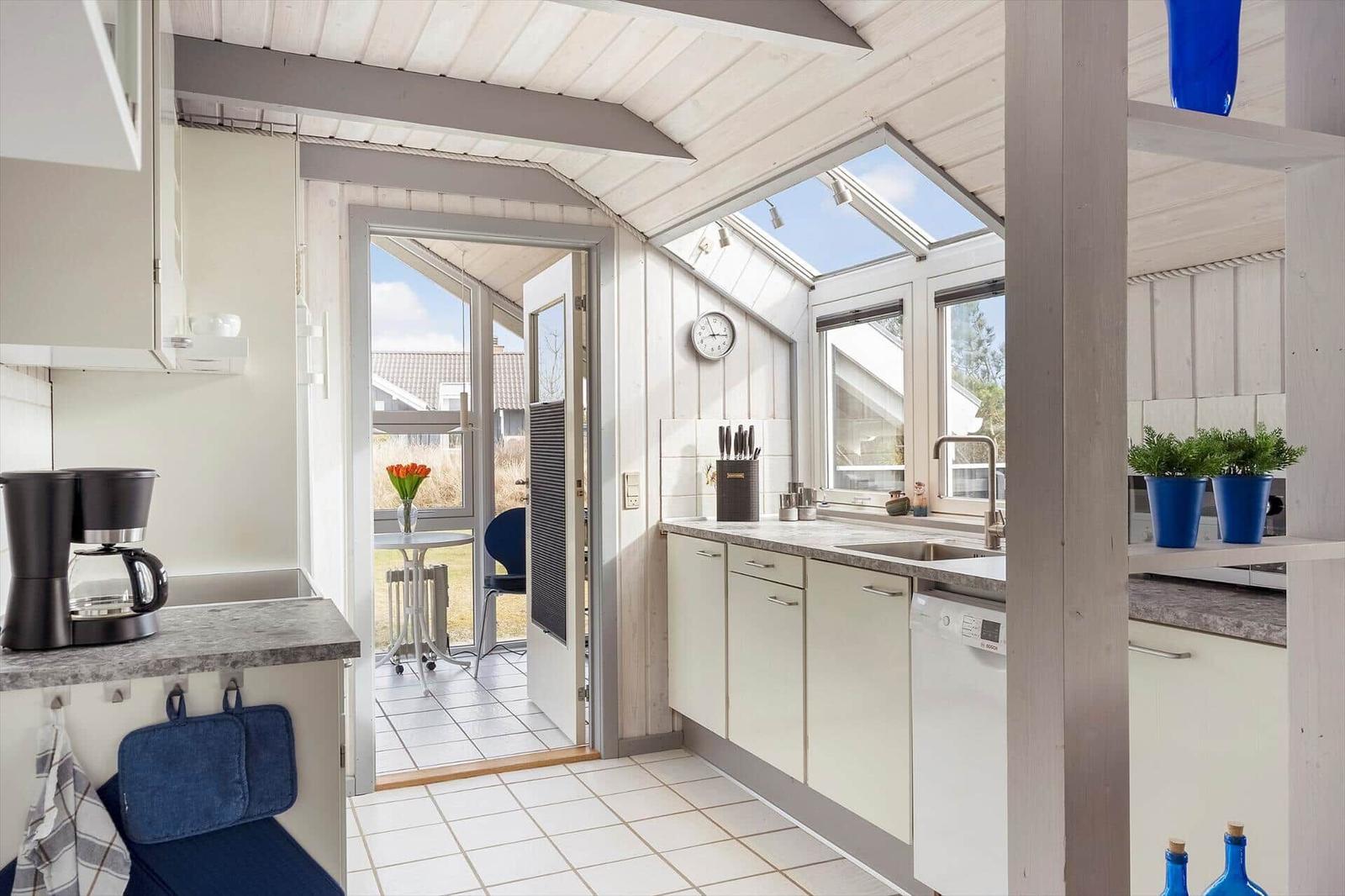 Küche mit Blick auf Terrasse und Dachfenster. Weiße Schränke, Arbeitsplatte und Bodenfliesen.