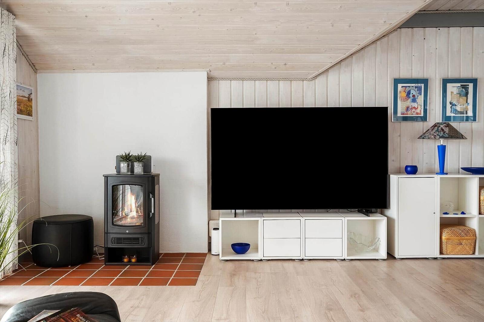 Wohnzimmer mit Kamin, TV und weißen Schränken. Holzdecke und Terrakottaboden.