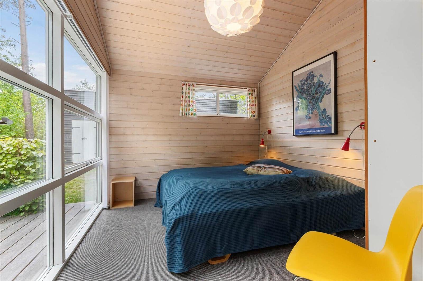 Schlafzimmer mit Holzwand, großem Fenster und blauer Bettdecke.