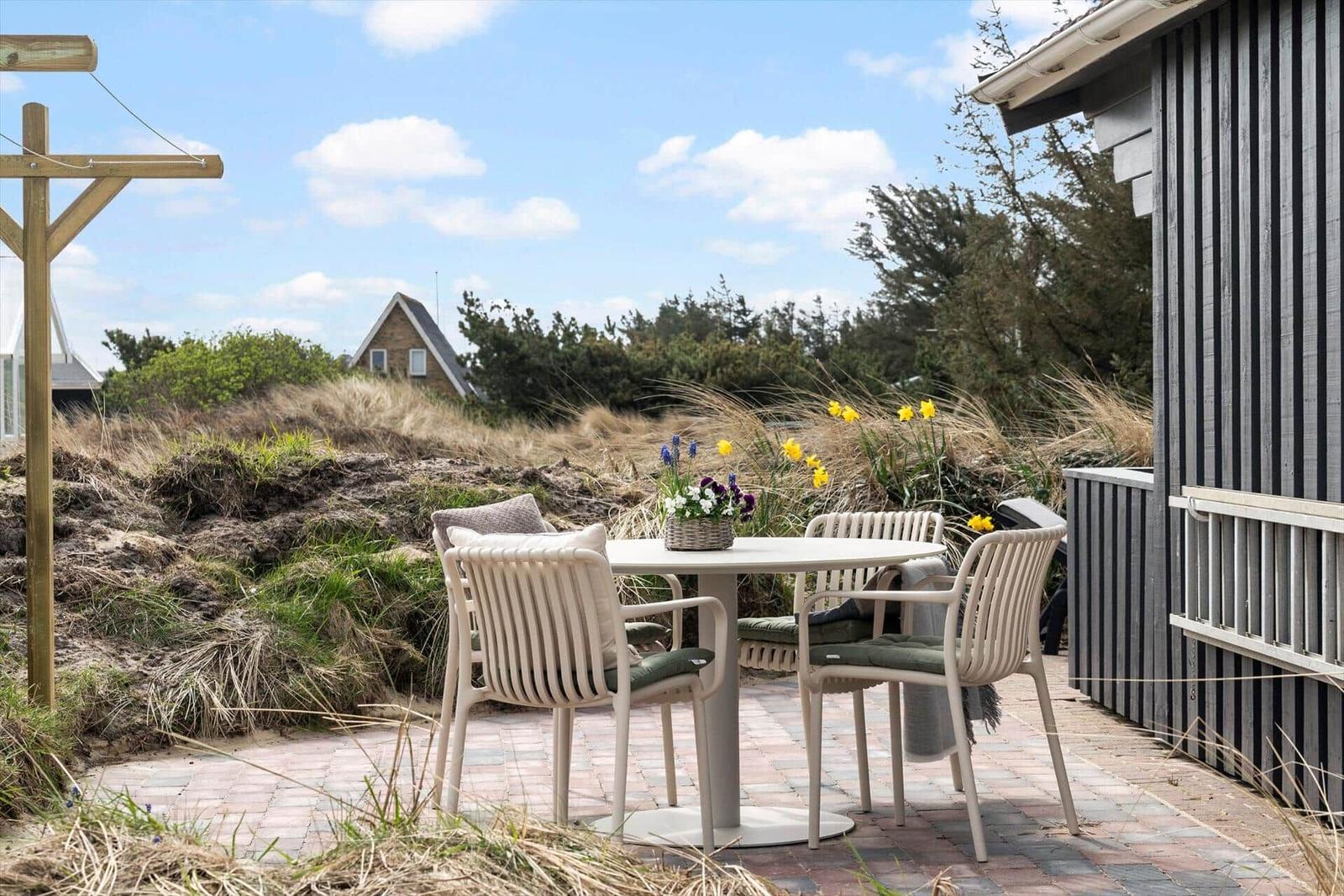 Terrasse mit Tisch und Stühlen, Blick auf Dünen und Haus.