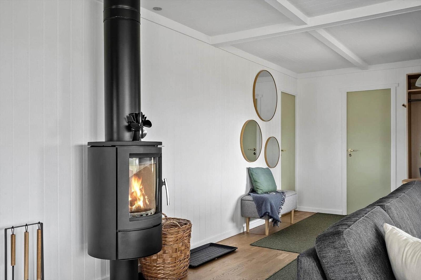 Wohnraum mit Kaminofen, Wandspiegeln und Sofa. Holzboden und weiße Wände.