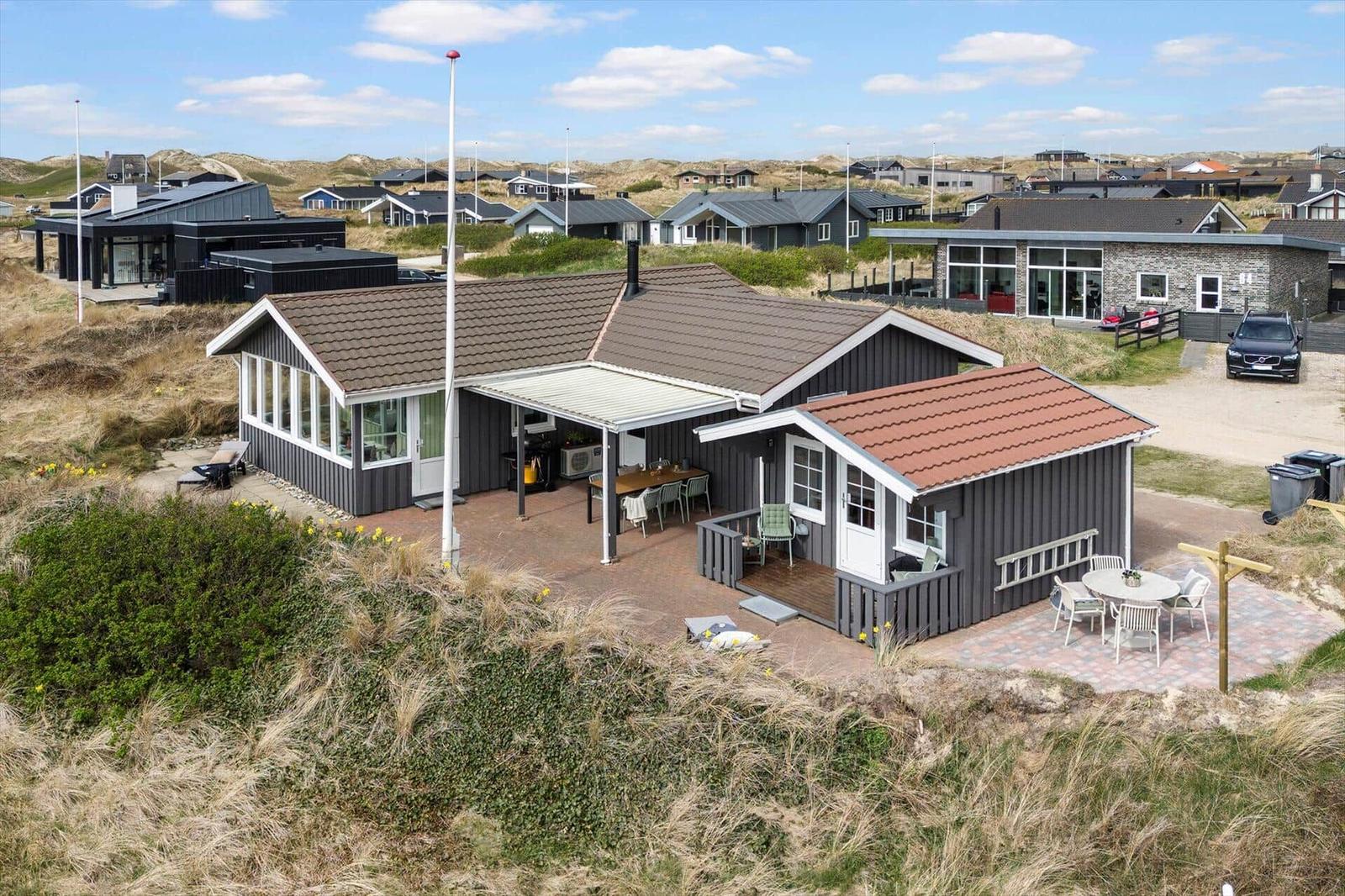 Haus mit Terrasse und Garten, umgeben von Dünen und weiteren Häusern.