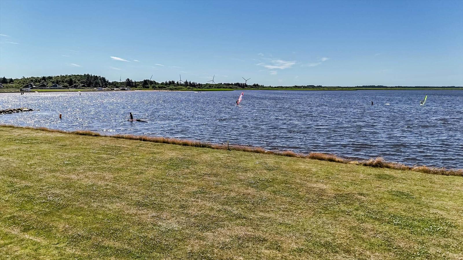 A windsurfer sails on a lake with a green shoreline in the background.