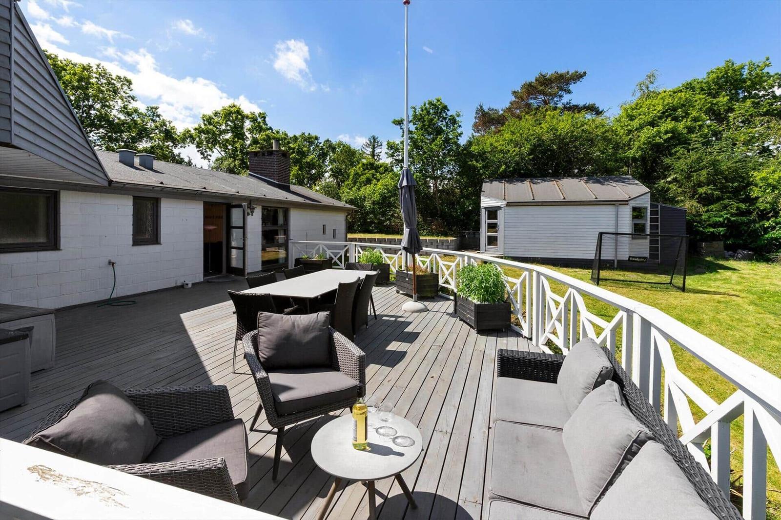 Deck with seating, table, and garden. Background: house and trees.