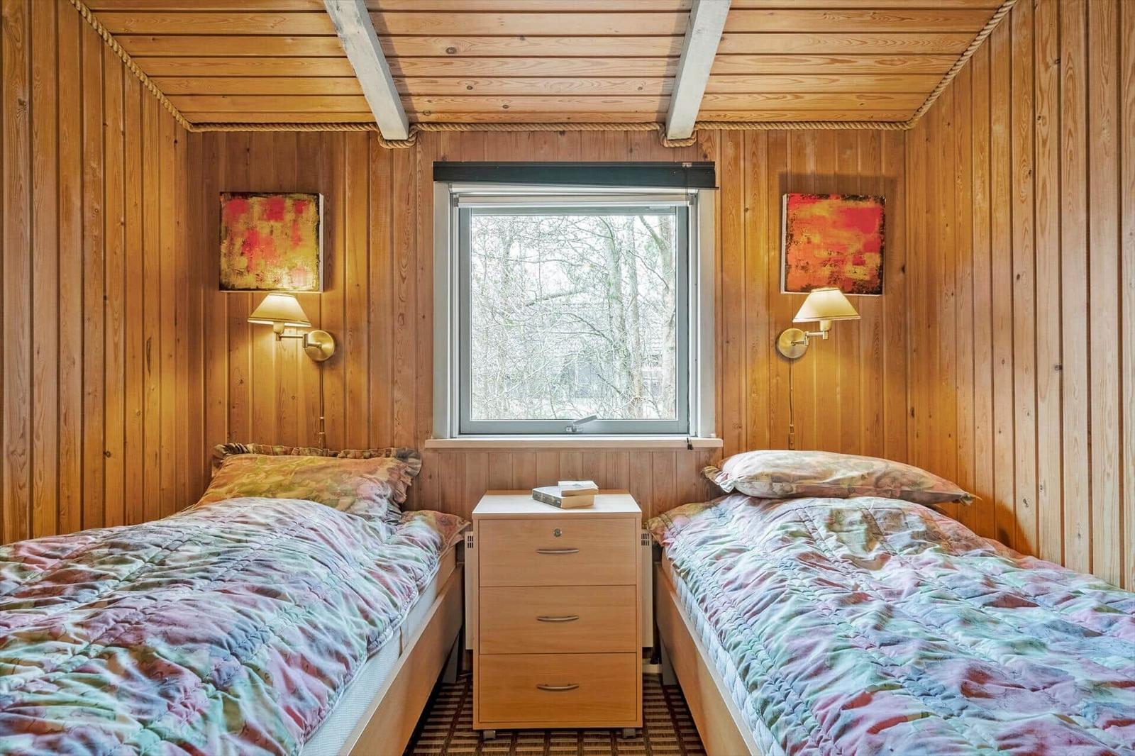 Zwei Betten mit bunten Decken, ein Nachttisch und ein Fenster mit Blick auf Bäume.