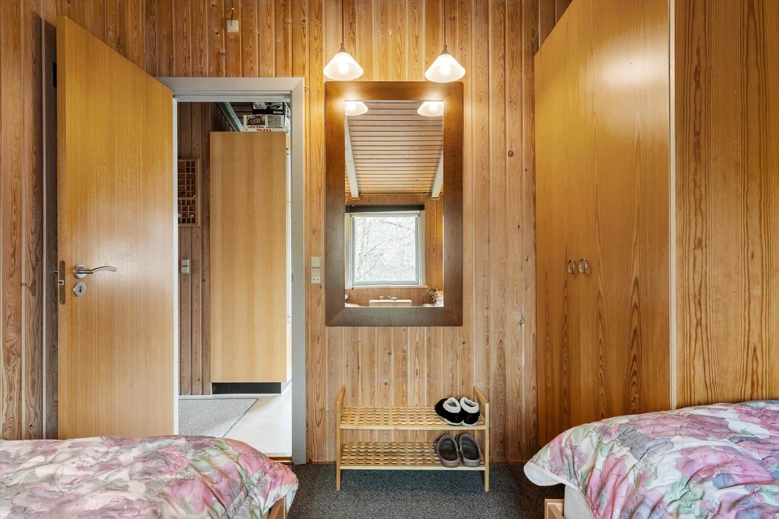 Zimmer mit Holzwand, Spiegel, Schuhschrank und zwei Betten mit Blumenbezügen.