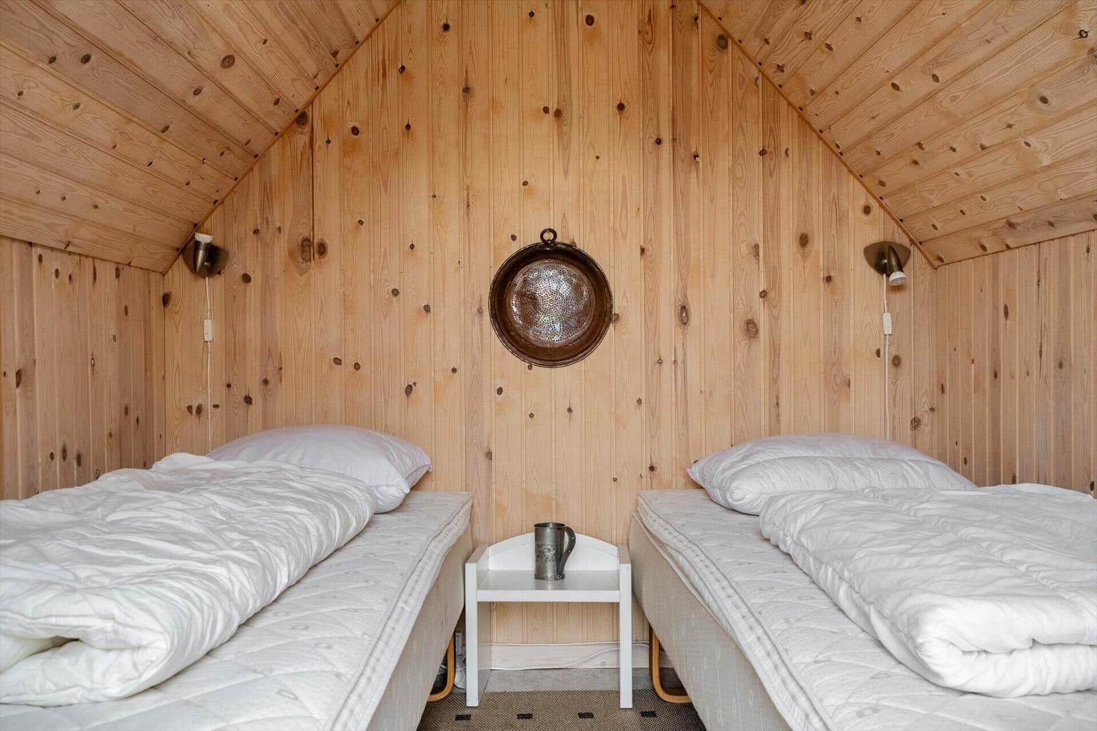 Zwei Betten mit weißen Decken, Holzwände und Decke, kleiner Tisch mit Tasse in der Mitte.