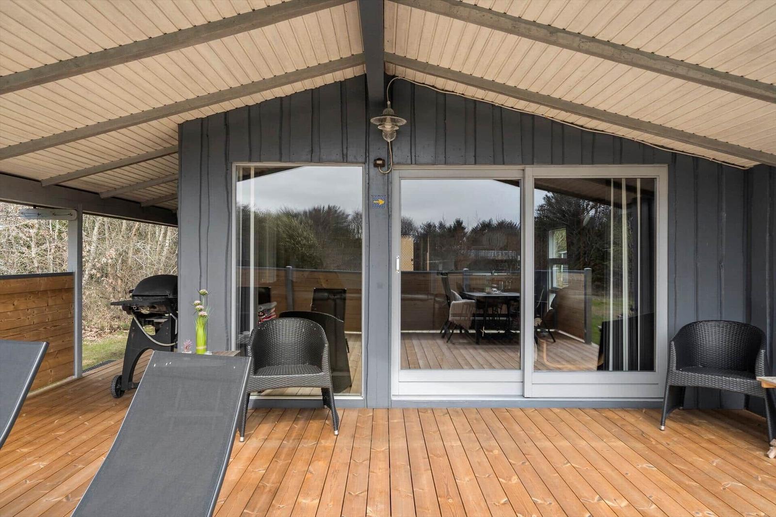 Terrasse mit Grill, Liegestuhl und Schiebetüren zu Wohnbereich.